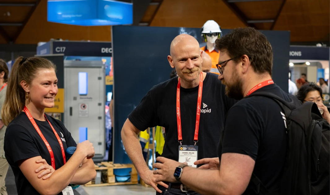 Rapid Global team members talking with a visitor at a trade show booth